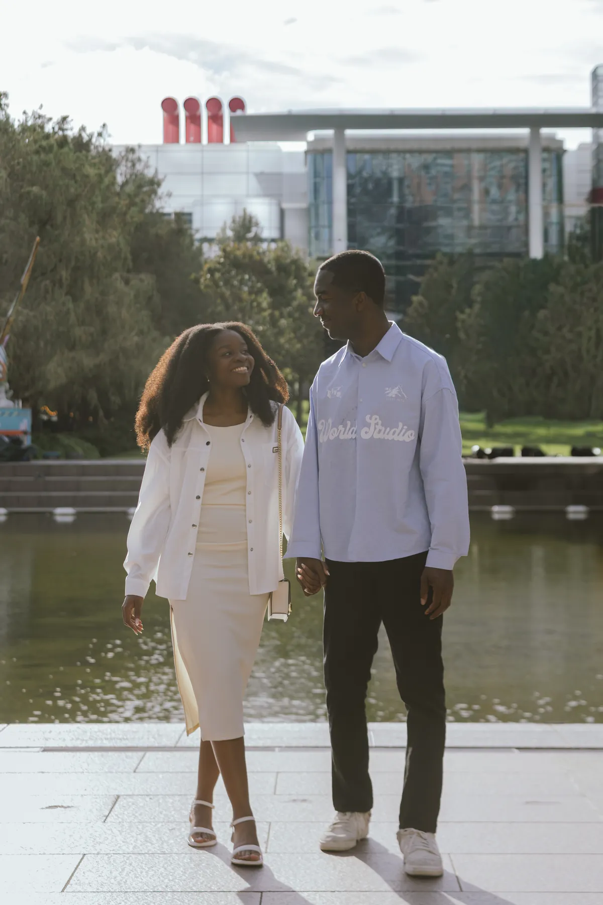 Jeremy and Afriyie walking hand in hand beside the water, smiling at each other