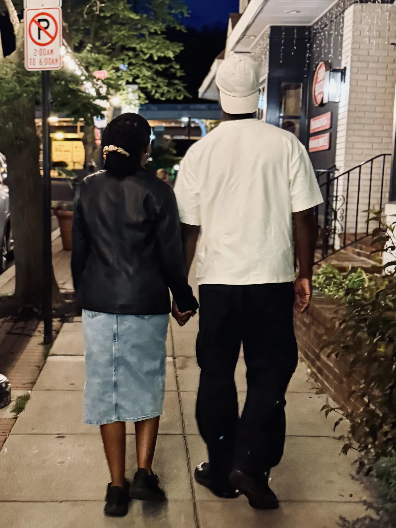 Jeremy and Afriyie walking hand in hand down a street at night, seen from behind